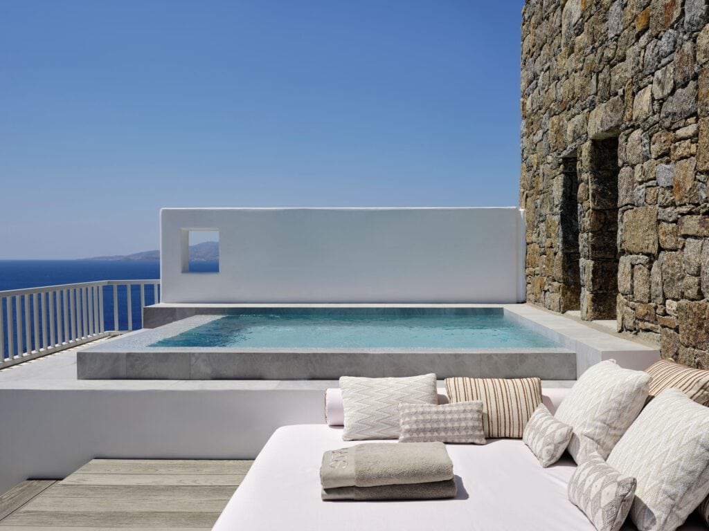 Infinity-Pool mit Blick auf das Meer, weiße Architektur, Sonnenschein, entspannte Atmosphäre, Lounge.