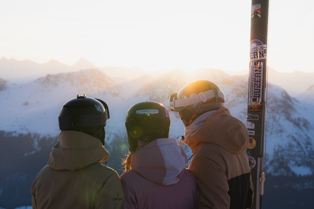 Drei Skifahrer mit Helmen blicken auf Bergpanorama bei Sonnenuntergang, Winterdestination Arosa Schweiz