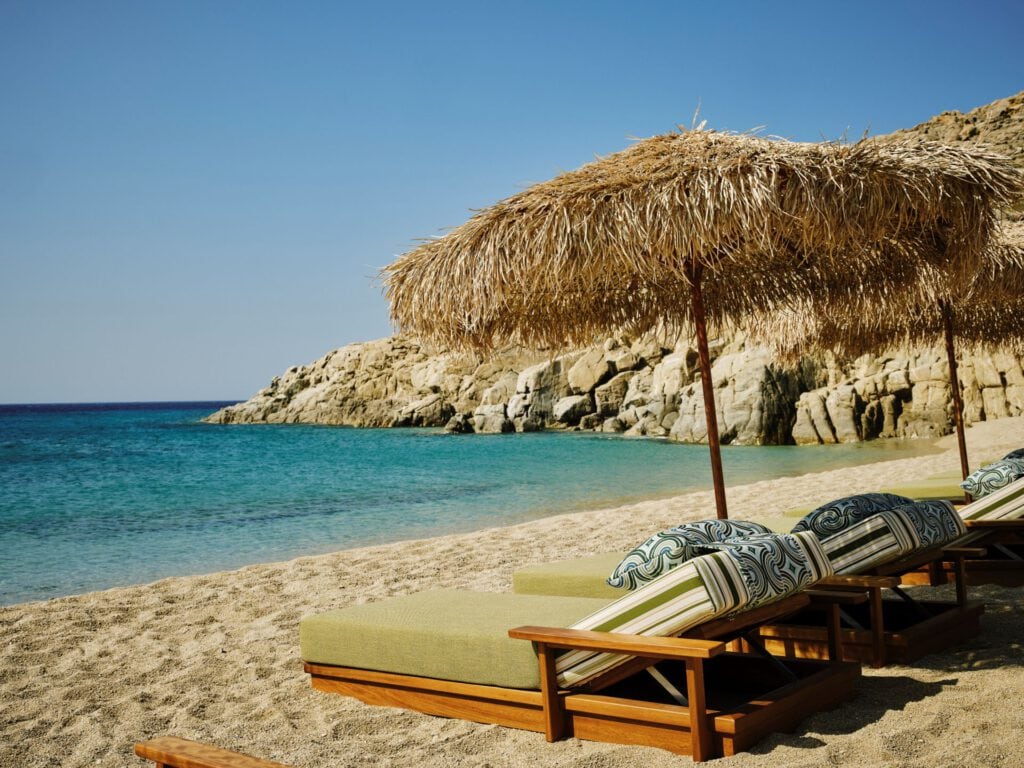 Myconian Collection – Sonnenliegen mit Strohschirm am Privatstrand, Luxusresort Mykonos Griechenland