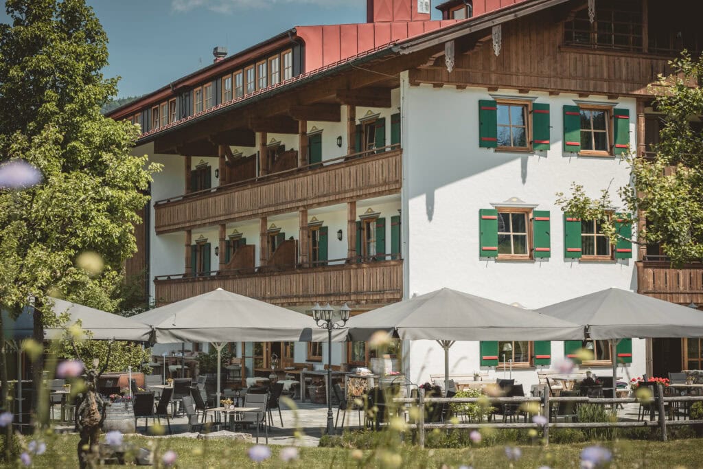 Traditionelles Alpenhotel mit Holzbalkonen und grünen Fensterläden, Sonnenterrasse im Garten