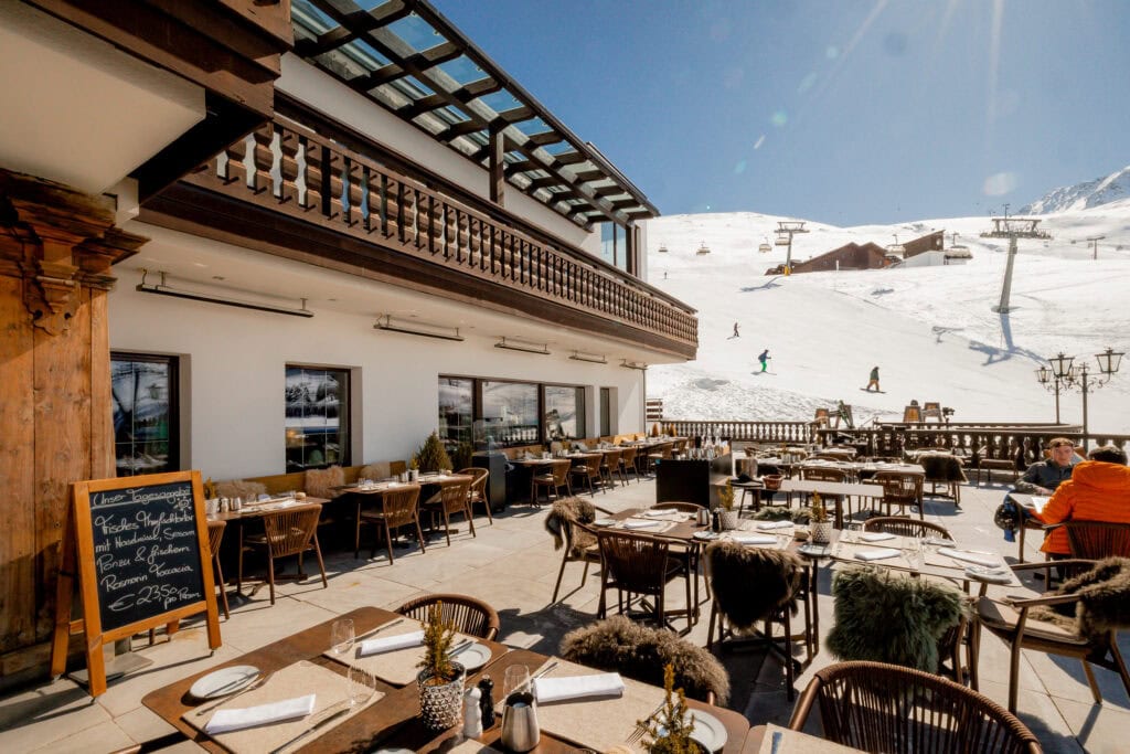 Sonnenterrasse eines Skihotels mit gedeckten Tischen und Blick auf Skipiste und Sessellift, Luxusresort Alpen