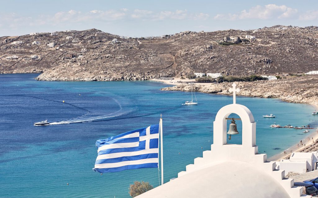 Myconian Villa Collection – Blick auf Bucht mit Glockenturm und griechischer Flagge, Luxushotel Mykonos