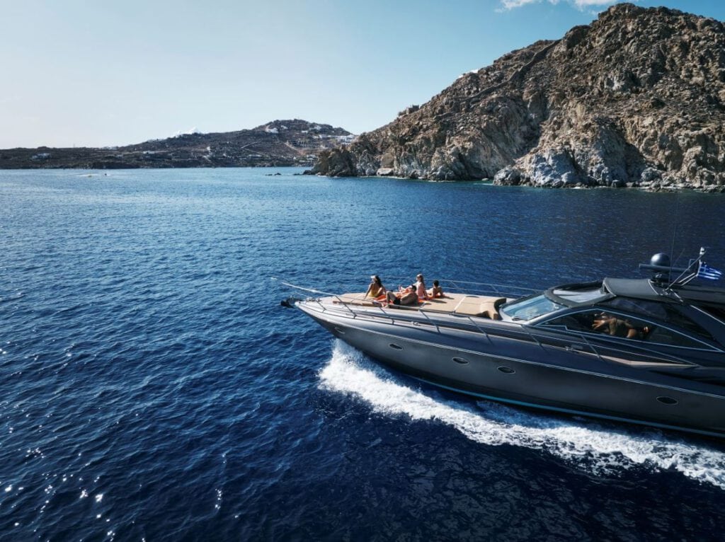 Luxusyacht vor griechischer Felsenküste mit Gästen an Deck, Destinationsmarketing Griechenland