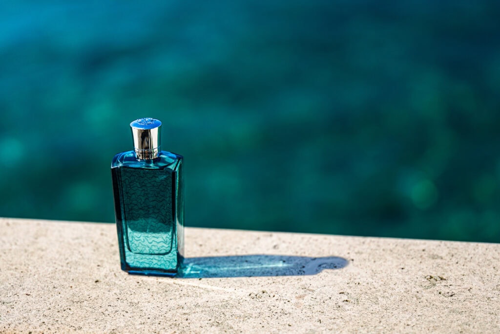 Eleganter Parfumflakon von The Merchant of Venice auf Steinmauer vor türkisblauem Wasser