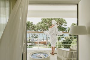 Frau in Bademantel auf Balkon mit Meerblick und Palmen.