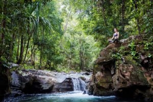 Frau meditiert auf einem Felsen neben einem Wasserfall im Dschungel.